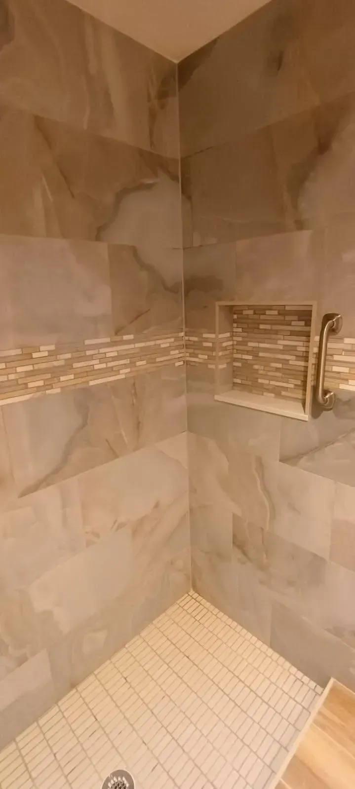 Corner shower with beige marble-look tiles, a mosaic tile border, and a built-in shelf.
