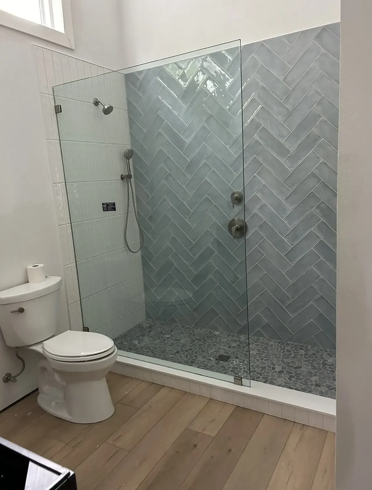 Bathroom with a glass-enclosed shower, herringbone-patterned gray tile, pebble floor, and toilet.