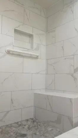 White tiled shower with built-in bench, shelf, and recessed niche. Pebble flooring.