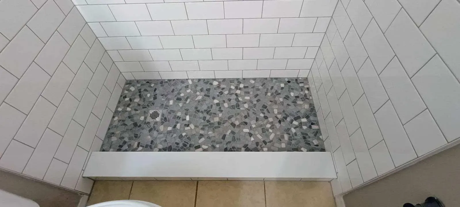 A shower stall with white tiled walls and a gray stone floor.