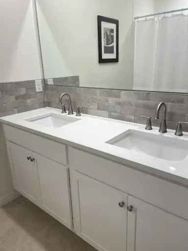 White double bathroom vanity with two sinks, gray backsplash, large mirror, and a framed picture.