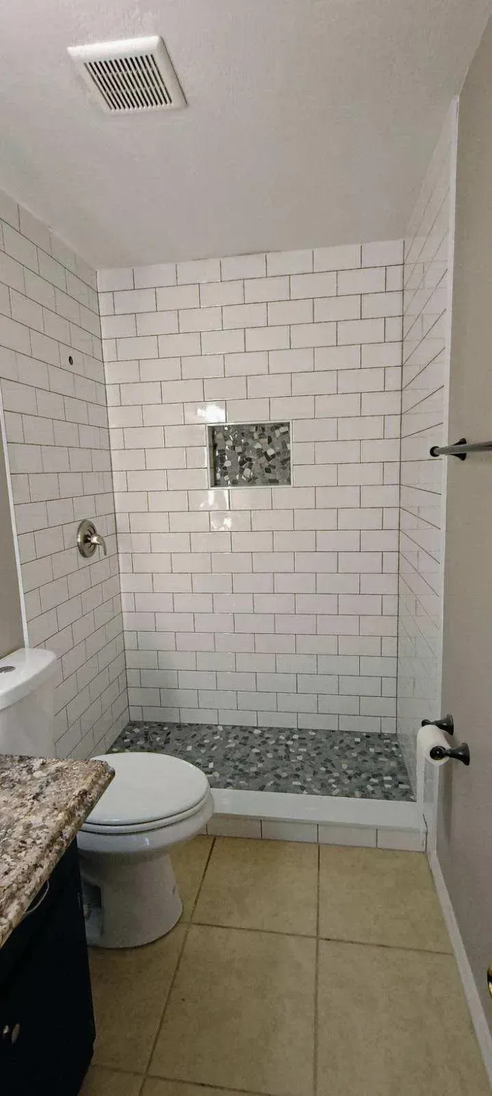 Bathroom with white brick-style shower, toilet, pebble shower floor, and granite countertop.