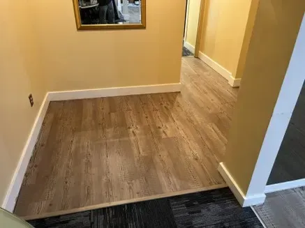 Hallway with light brown wood-look flooring, yellow walls, white baseboards, and a mirror.