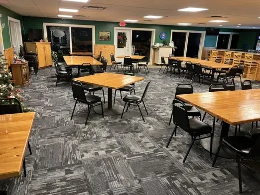 An empty dining room with wooden tables, black chairs, and a patterned carpet.