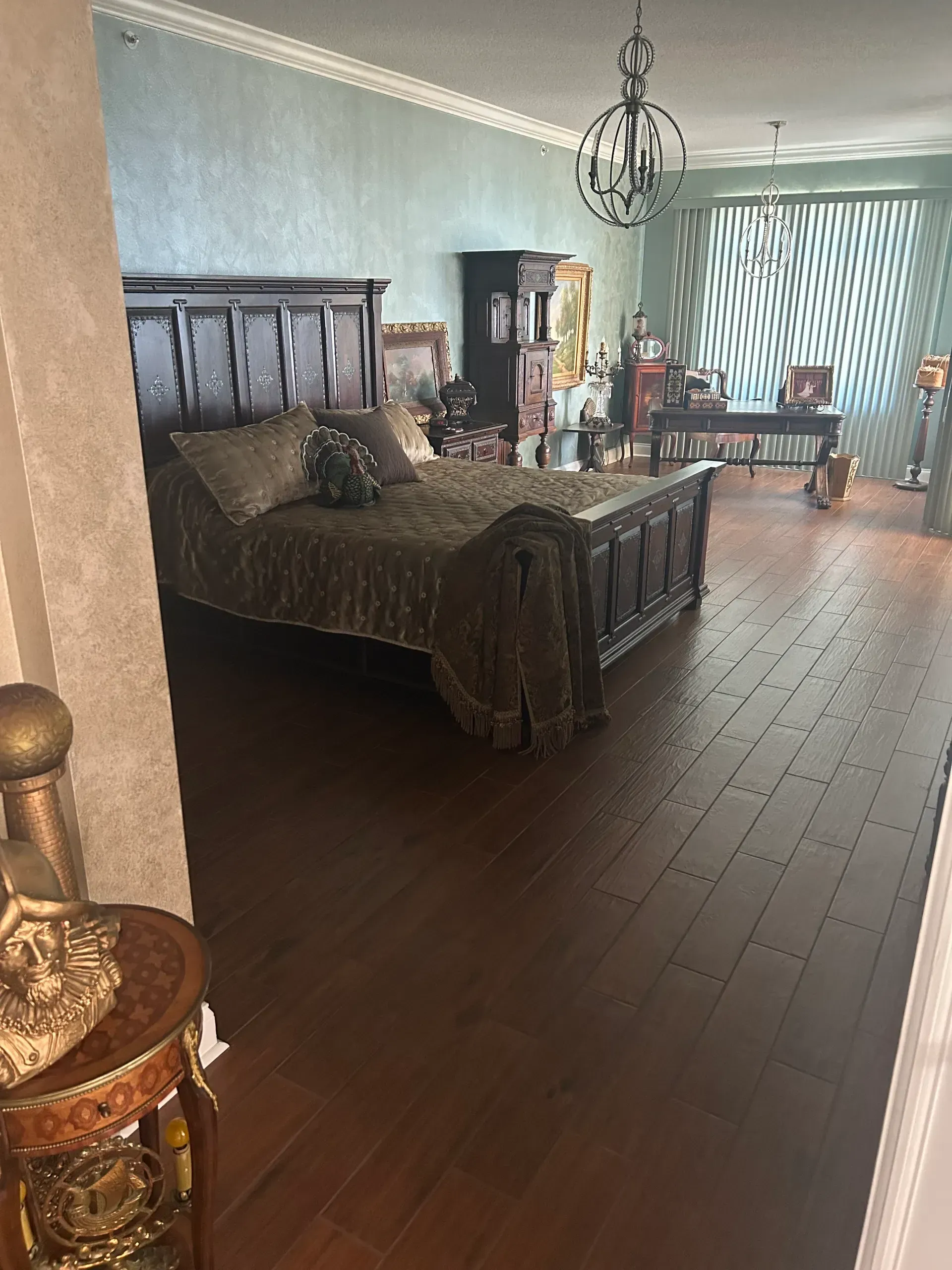 Bedroom with dark wood bed, hardwood floors, teal walls, and chandelier.