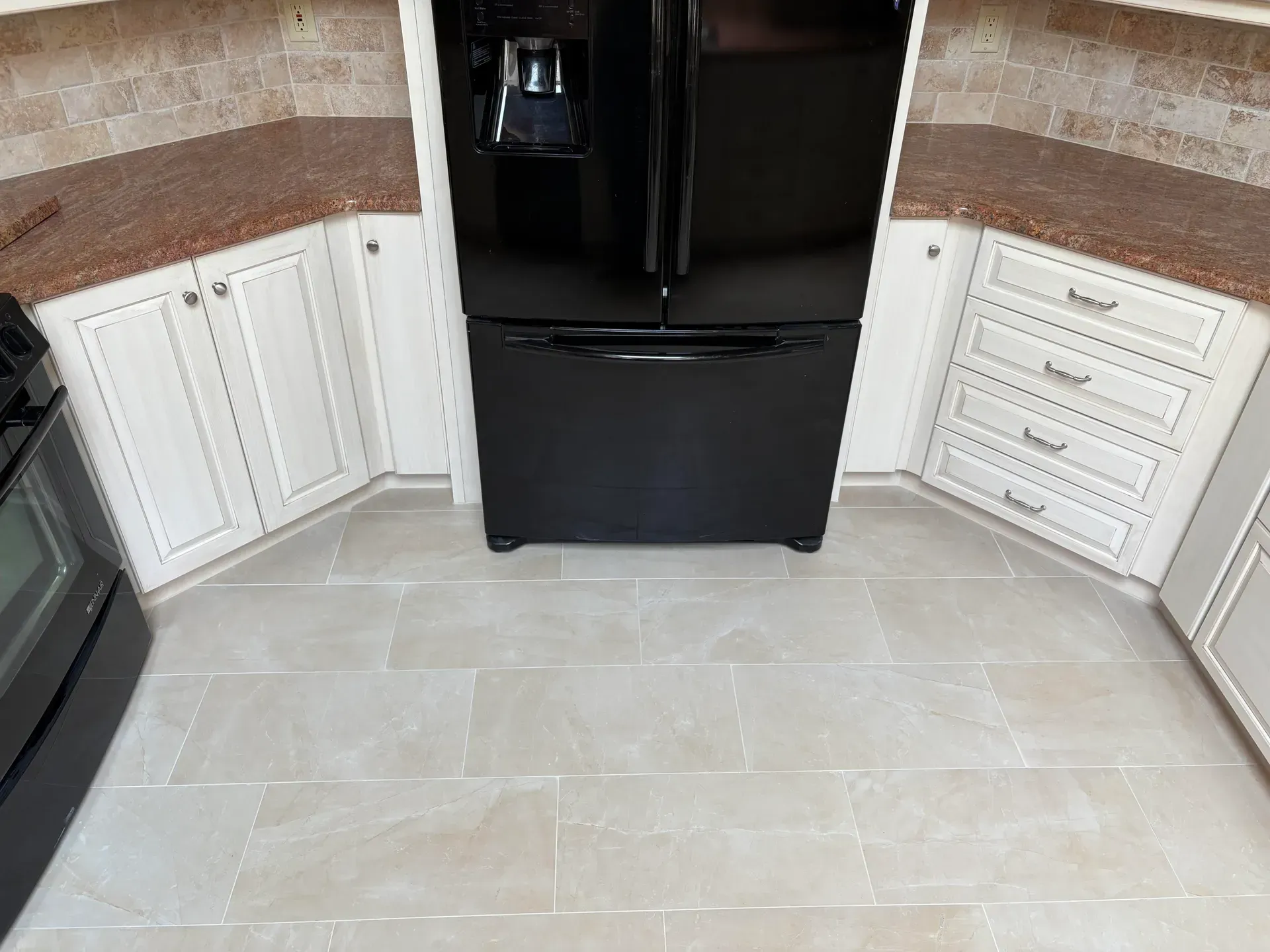 Kitchen with a black refrigerator centered between white cabinets and a tile floor.