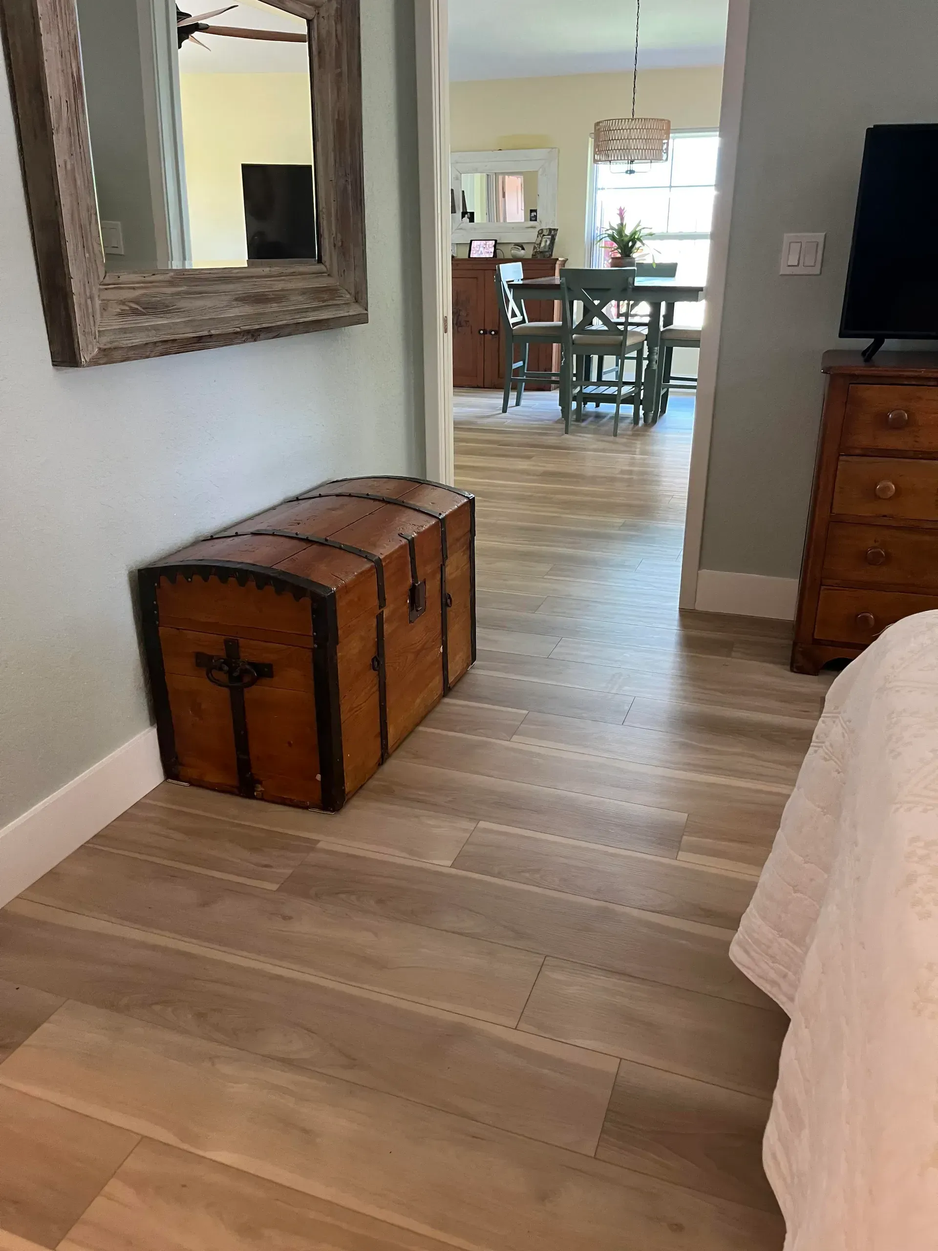 Wooden trunk and mirror in a room with wood-look flooring. Doorway leads to a dining area.