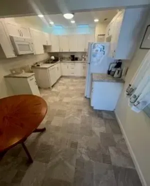 Kitchen with white cabinets, appliances, and gray tile flooring; a wooden table sits in the foreground.