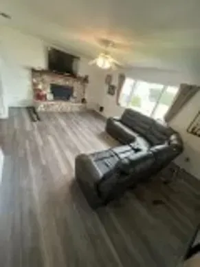 Living room with gray wood floors, black sectional, fireplace, and TV.