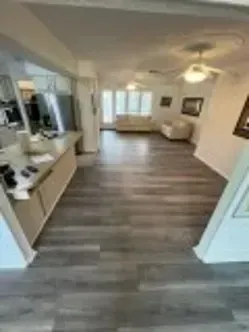 Wide-angle view of a home interior, featuring a kitchen and living room with wooden floors.