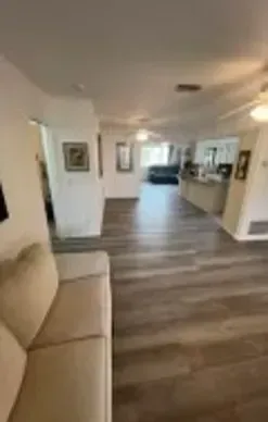 Beige sofa in a living room with wood-look flooring and a view to kitchen and hallway.