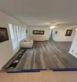 Spacious living room with gray wood floors, white walls, two white couches, and windows.