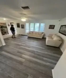Living room with gray wood-look flooring, two sofas, windows, and a person in the background.