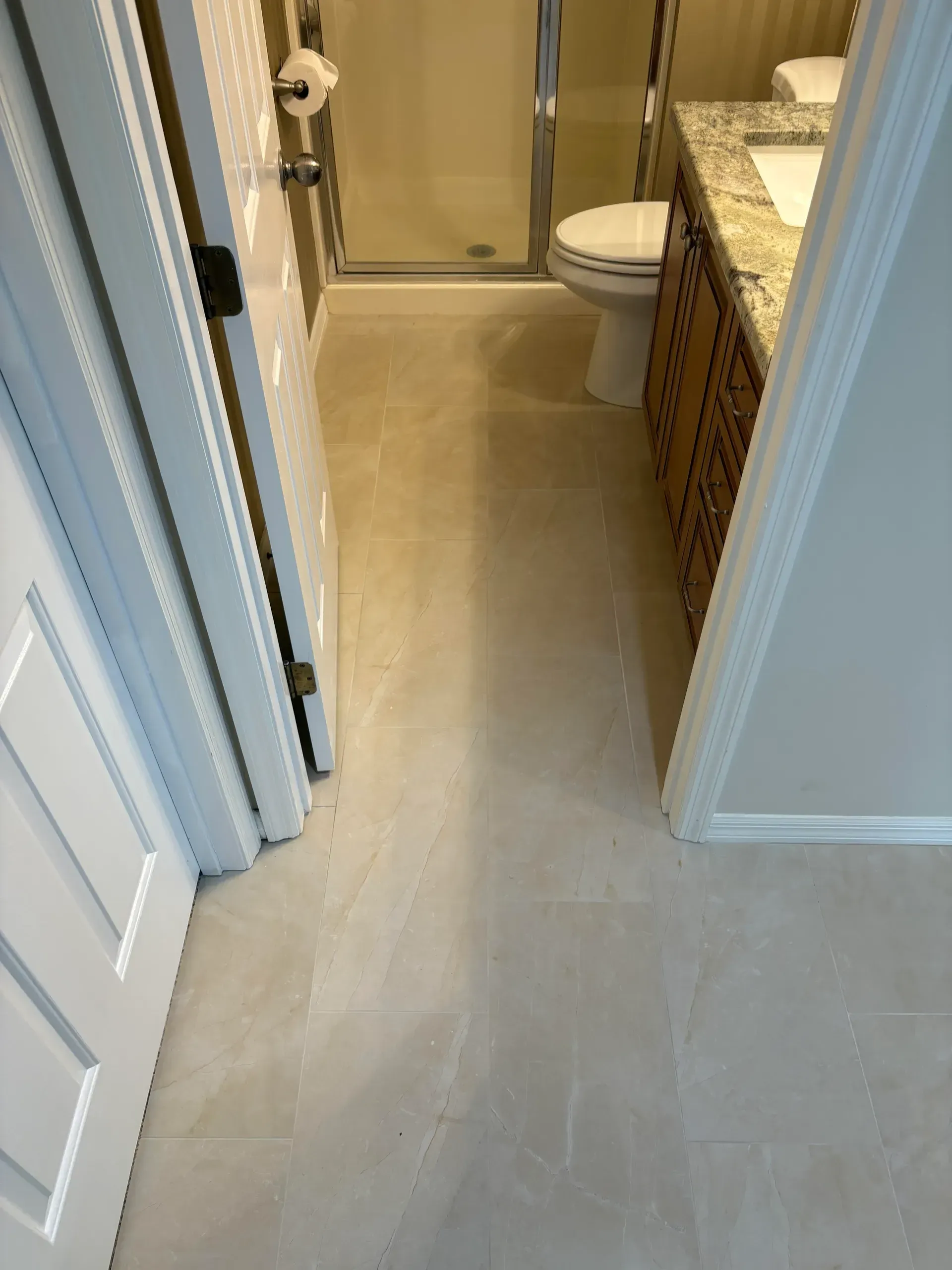 Bathroom with light-colored tile flooring, vanity with granite countertop, toilet, and shower with glass doors.