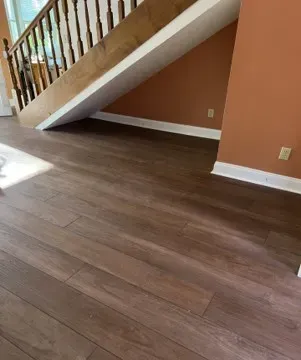 Wooden floor with stairs leading up, orange wall, white baseboards.