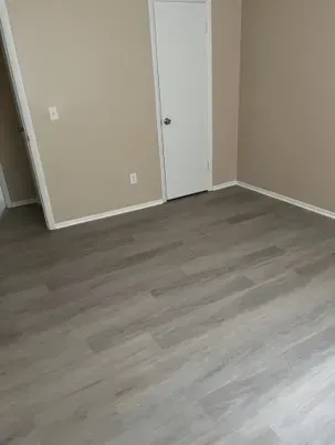 Empty room with gray wood-look flooring, beige walls, white door, and white trim.