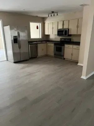Empty kitchen with stainless steel appliances, light cabinets, and gray flooring.