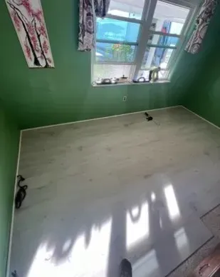 Green-walled room with a window, white flooring, and artwork. Natural light is reflected on the floor.