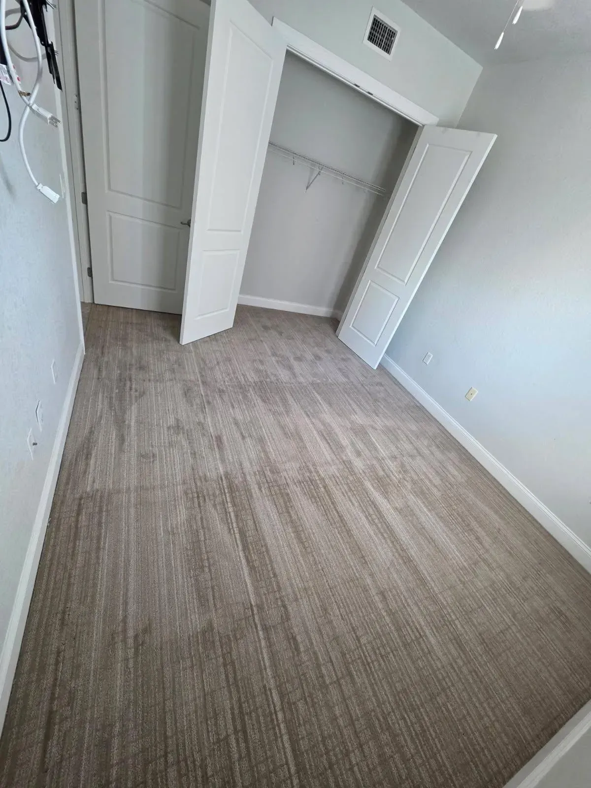 Empty bedroom with light brown carpet, white closet doors, and light gray walls.