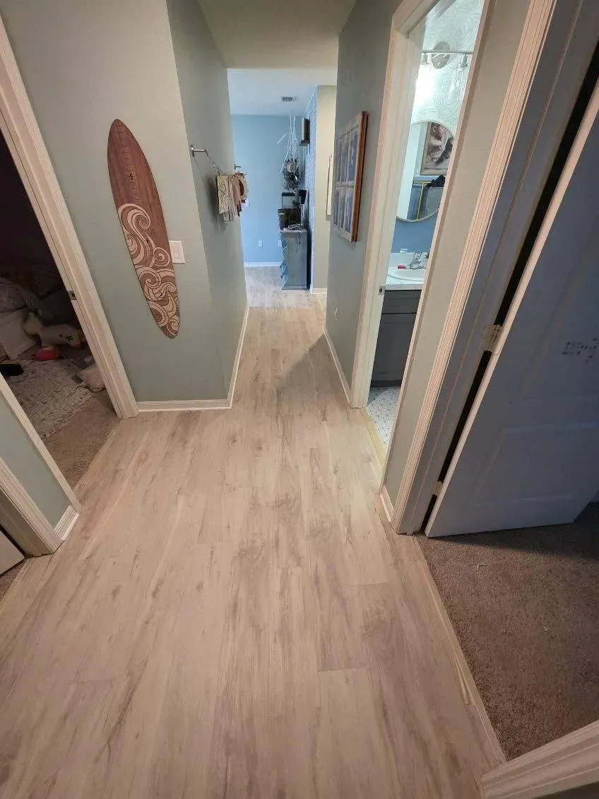 Hallway with light wood-look flooring and light blue walls. Doors on either side, one with a surfboard decoration.