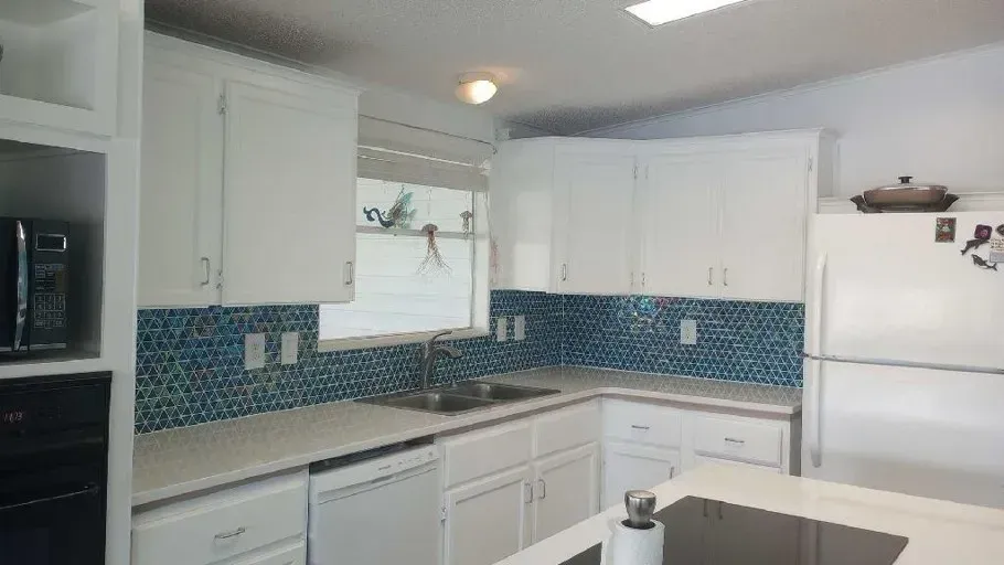 White kitchen with blue mosaic tile backsplash, white cabinets, and stainless steel sink.