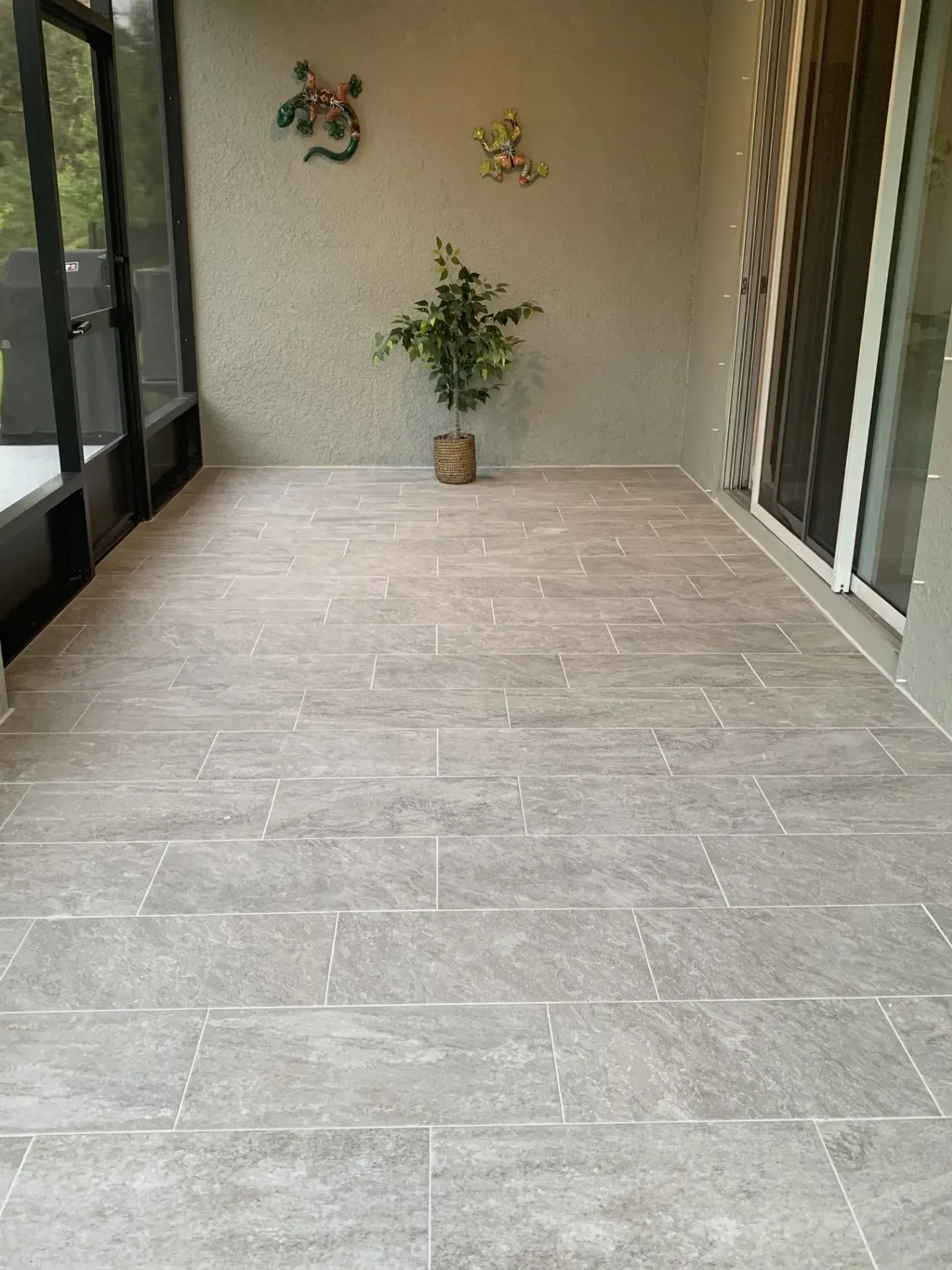 A screened-in porch with gray tiled floor, a potted plant, and wall decorations.