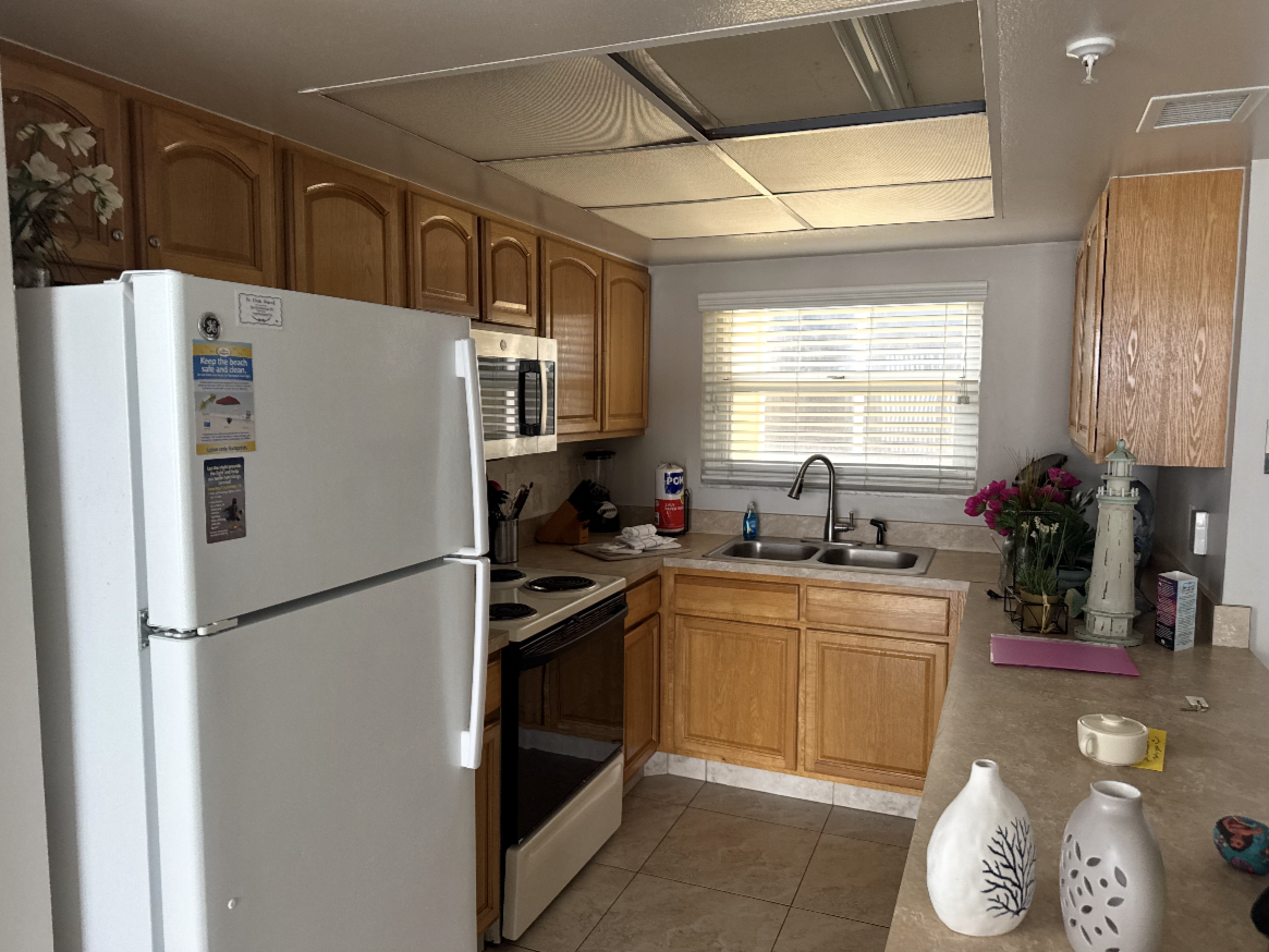 Small kitchen with white appliances, wood cabinets, tiled floor, and a window over the sink.