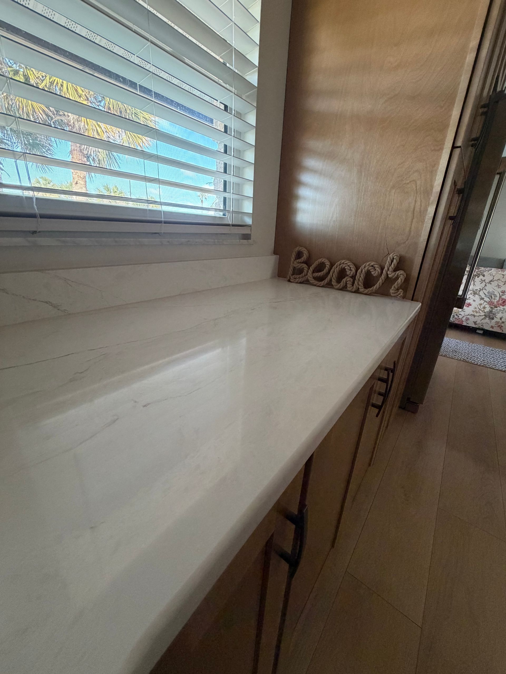 Narrow white countertop beside a window with blinds in a small kitchen or laundry area