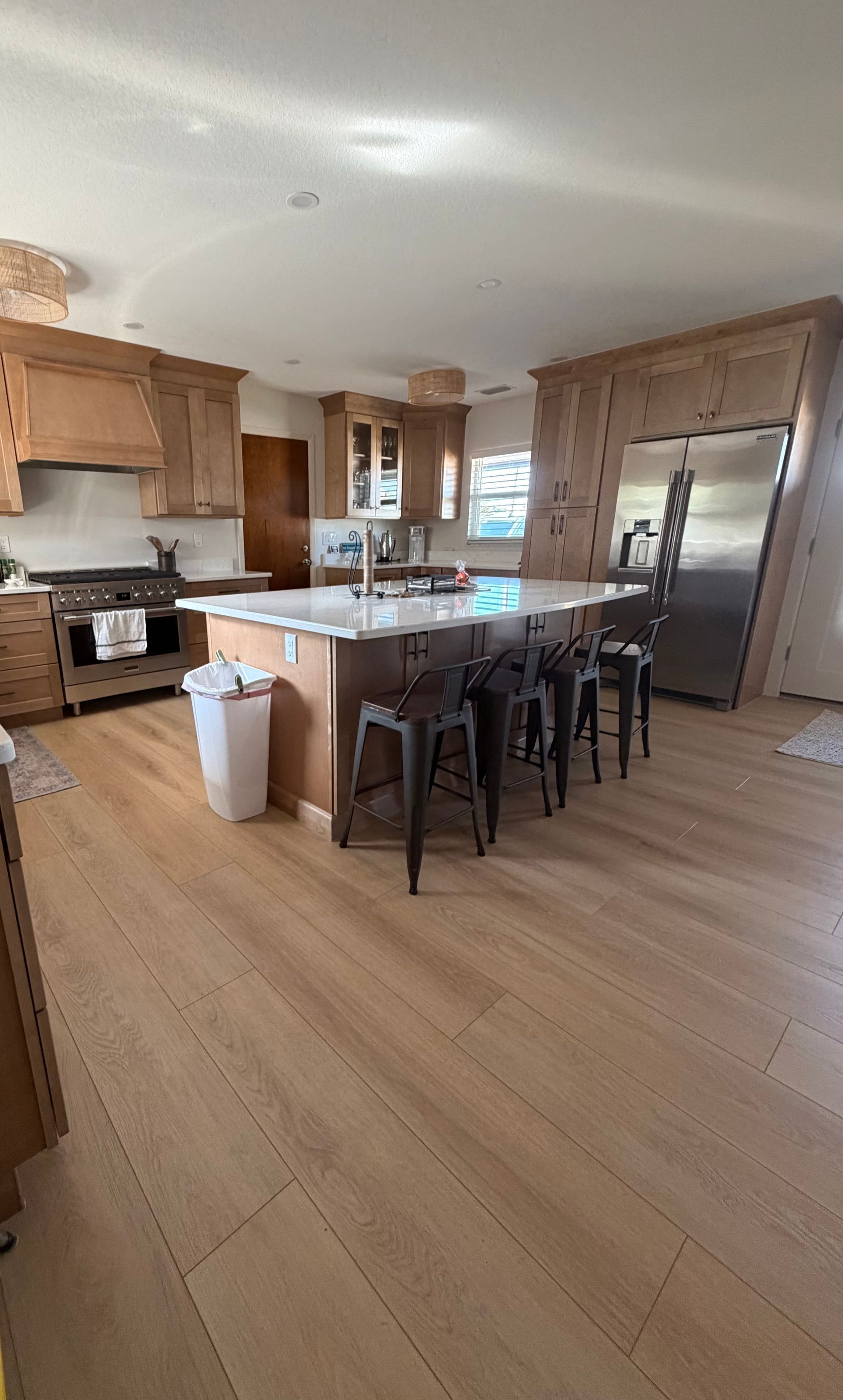 Spacious modern kitchen with wood cabinets, central island, barstools, and stainless steel refrigerator