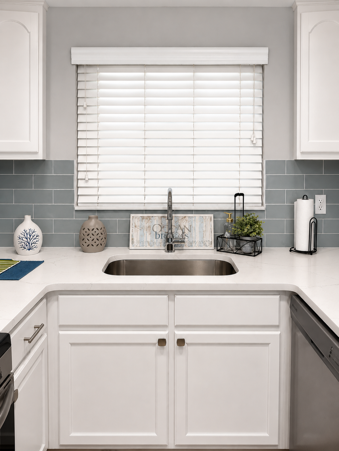 Bright white kitchen sink with window blinds, gray tile backsplash, and small countertop decor