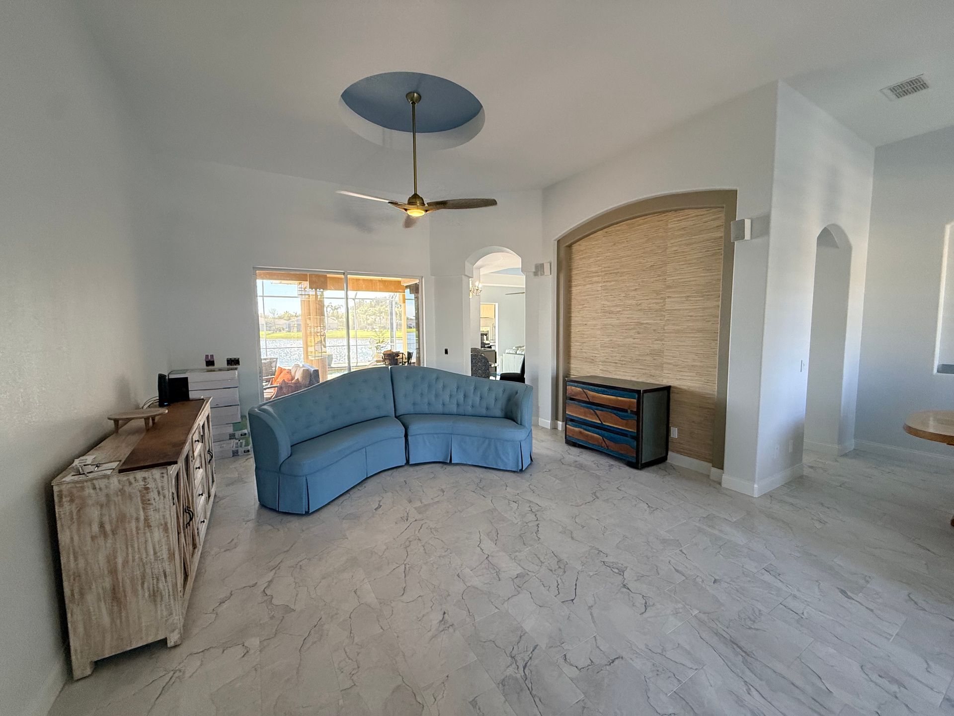 A spacious living room featuring a curved blue sofa, a rustic sideboard, and a large decorative wall niche.