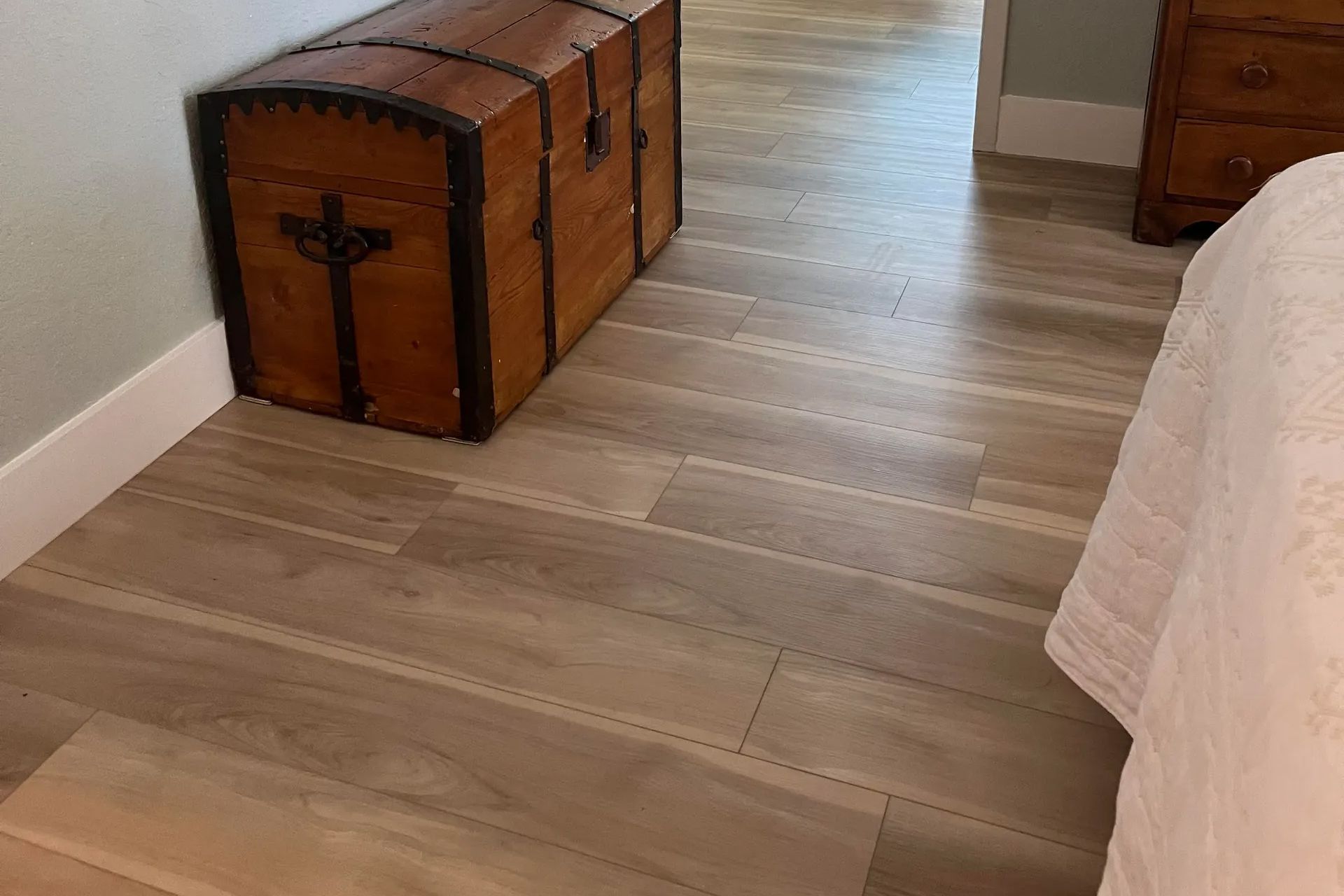 Wooden trunk bench with black cross on lid beside a bed in a bedroom with light wood flooring