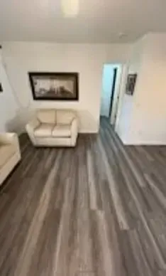 Living room with light-colored flooring, beige loveseat, and a framed picture on a white wall.