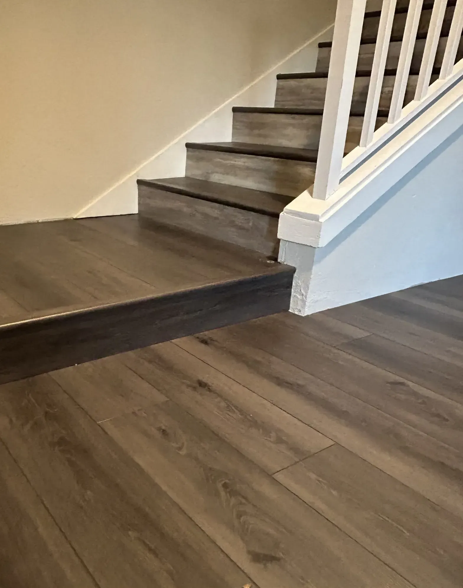 Interior staircase with dark wood steps and white railing beside wood-look flooring.