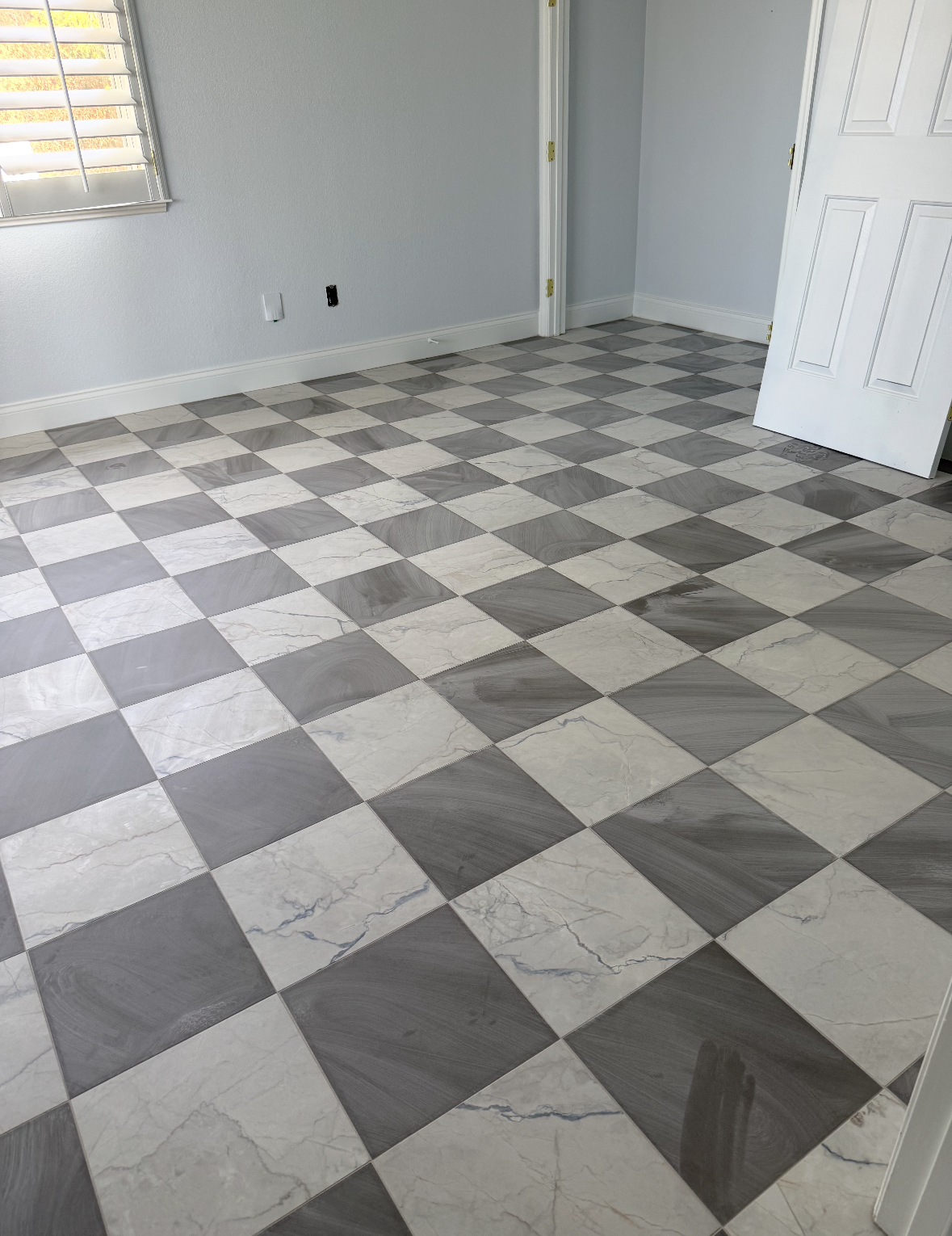 Empty room with black-and-white checkered tile floor and white walls, door ajar on the right.