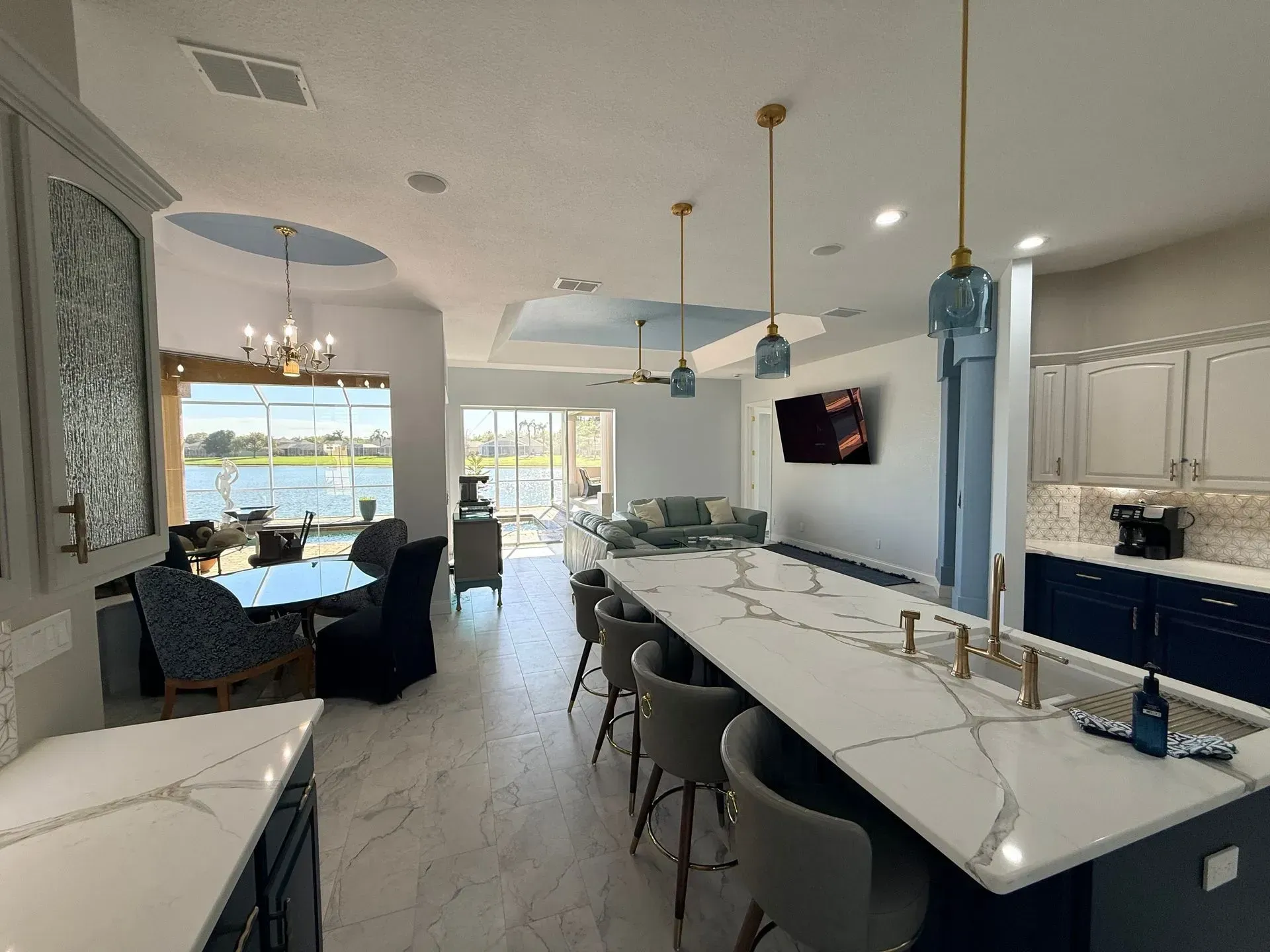 Bright modern kitchen with large island, bar stools, and open living area by a dining nook and patio doors.