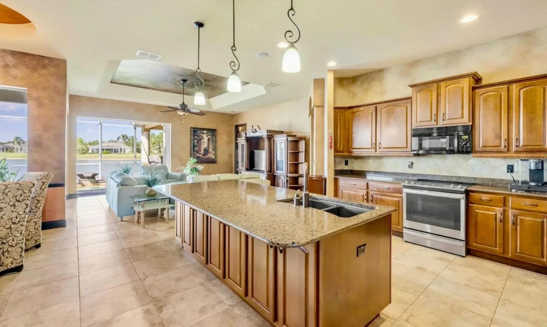 Spacious modern kitchen with granite island, wooden cabinets, pendant lights, and dining area.