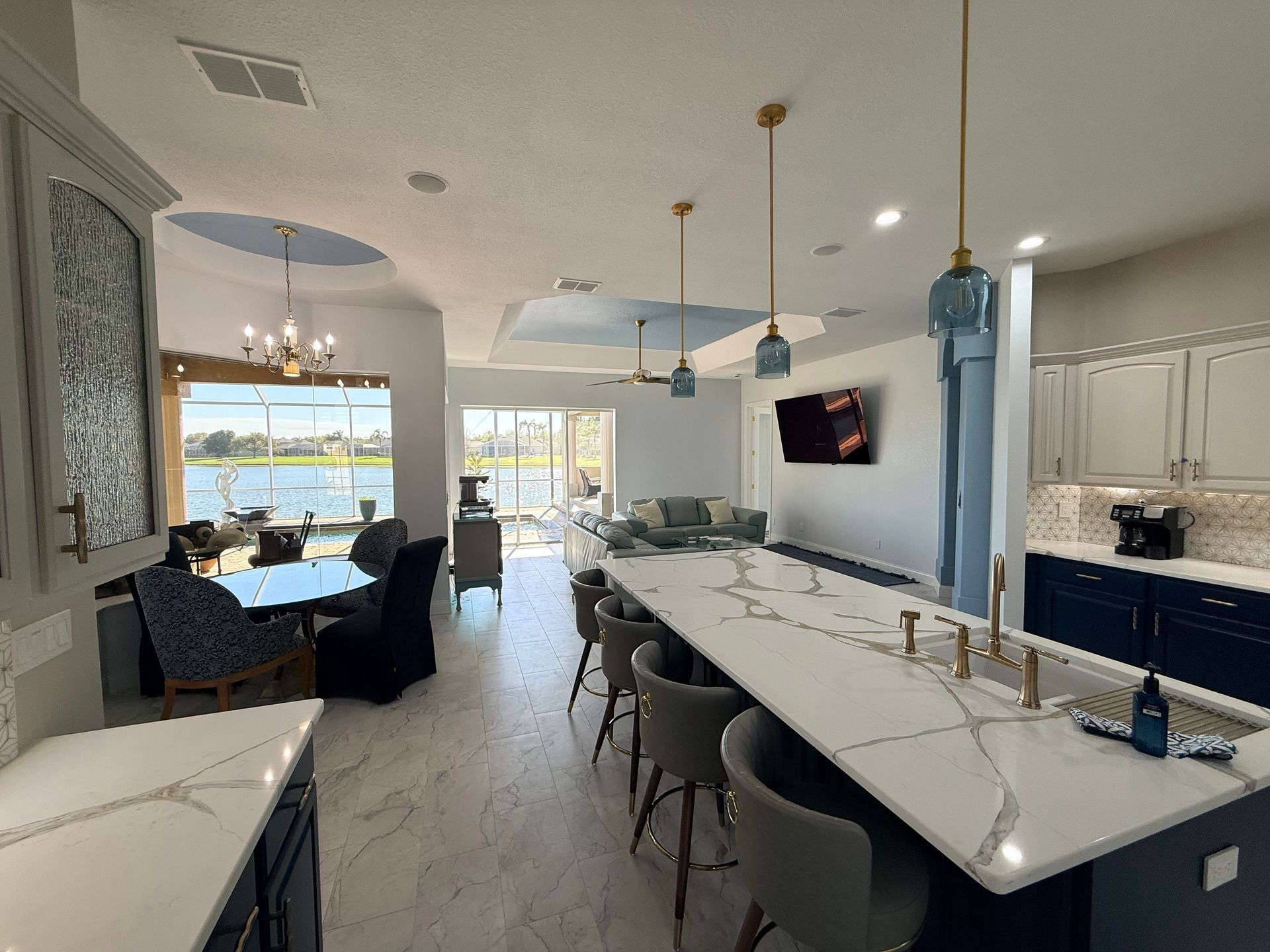 Modern kitchen and dining area with a long island, bar stools, and large windows overlooking water.