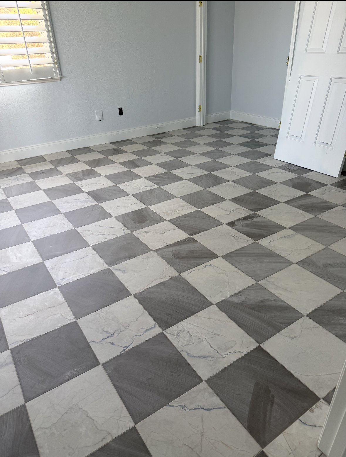 Empty room with gray-and-white checkered tile floor, white walls, and an open door.