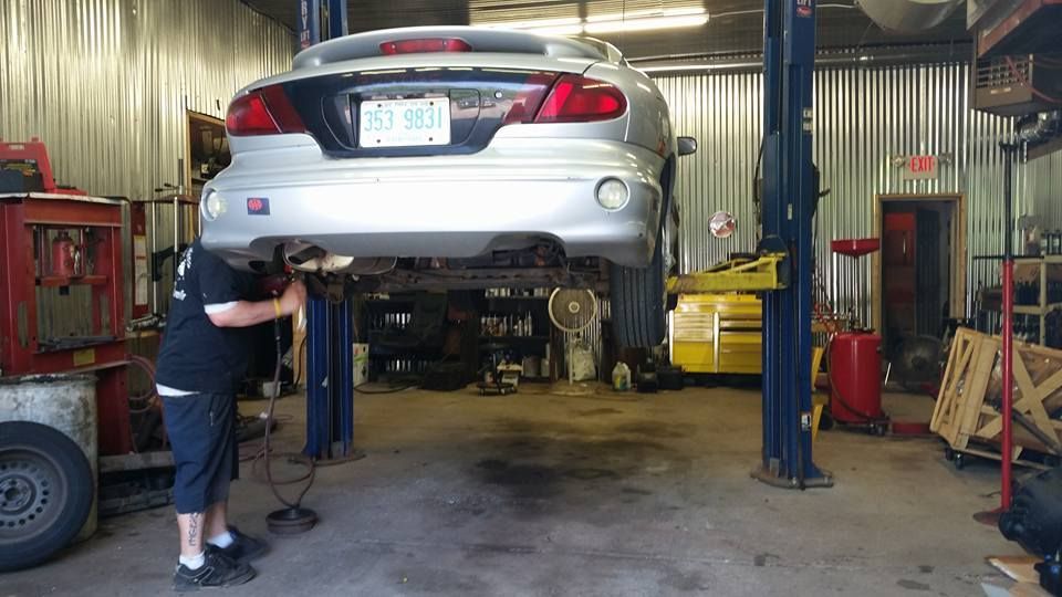 A man is working on a car on a lift in a garage.
