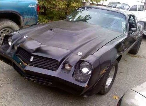 A black car is parked in a parking lot next to a truck.