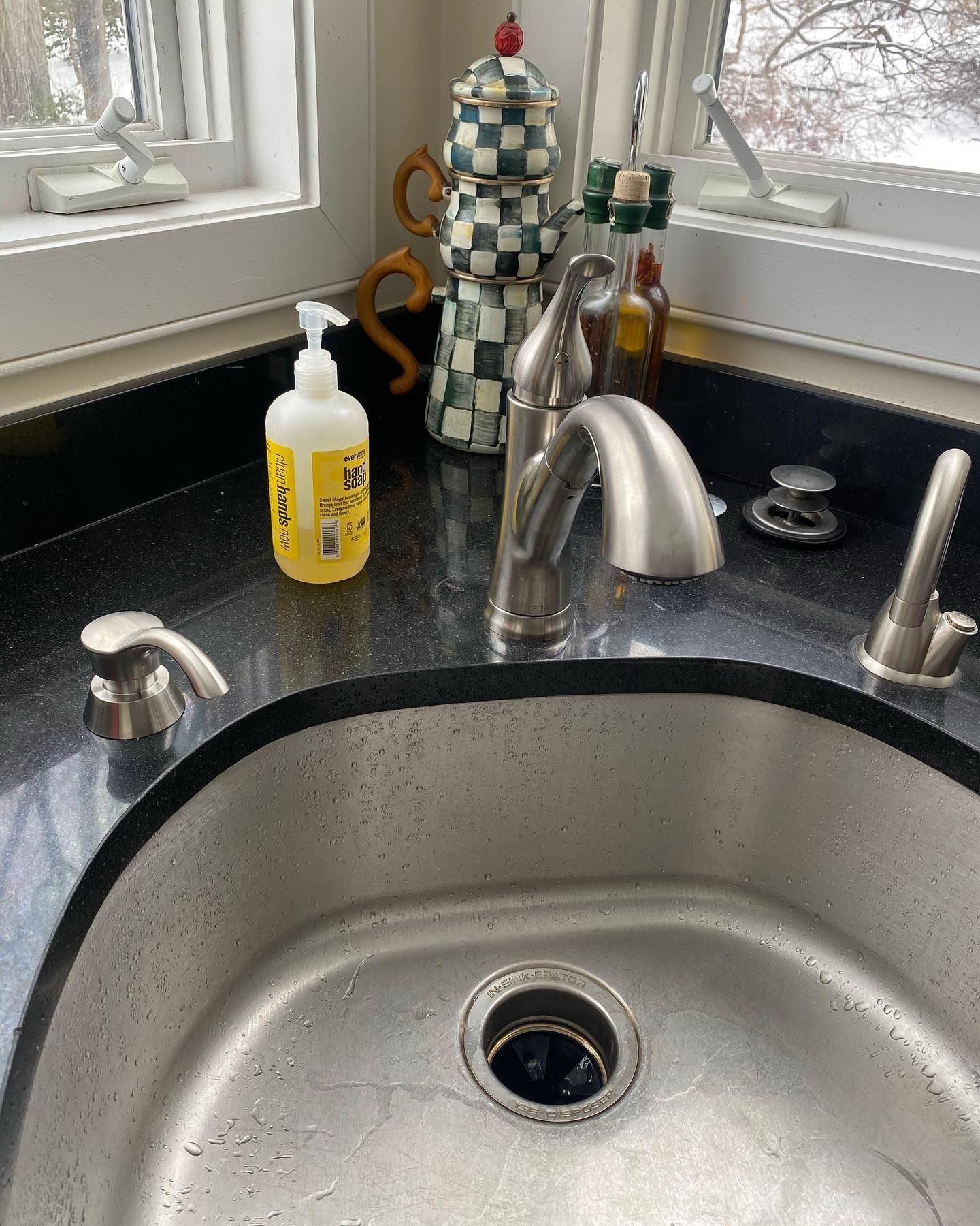 Stainless steel kitchen sink with black granite countertop, soap dispenser, and decorative items.
