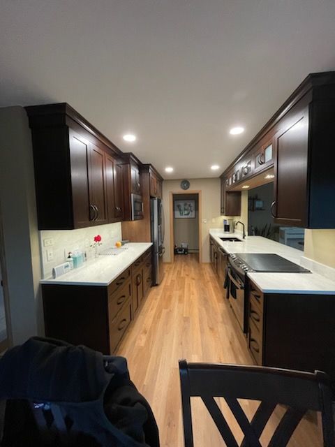 A long kitchen with dark cabinets and white counter tops