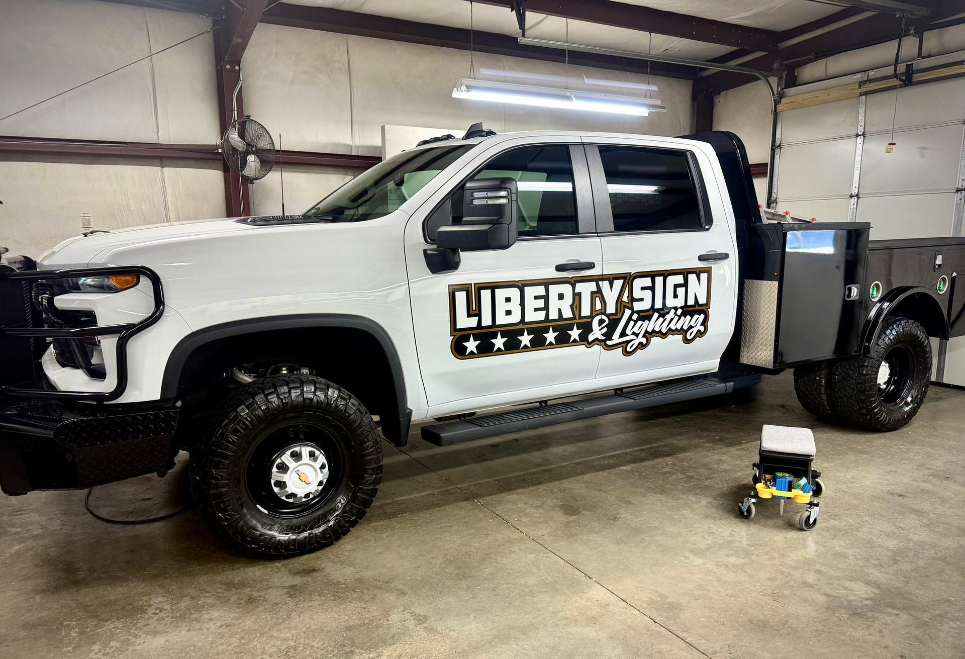 White Chevy truck with Liberty Sign & Lighting logo parked inside a garage.