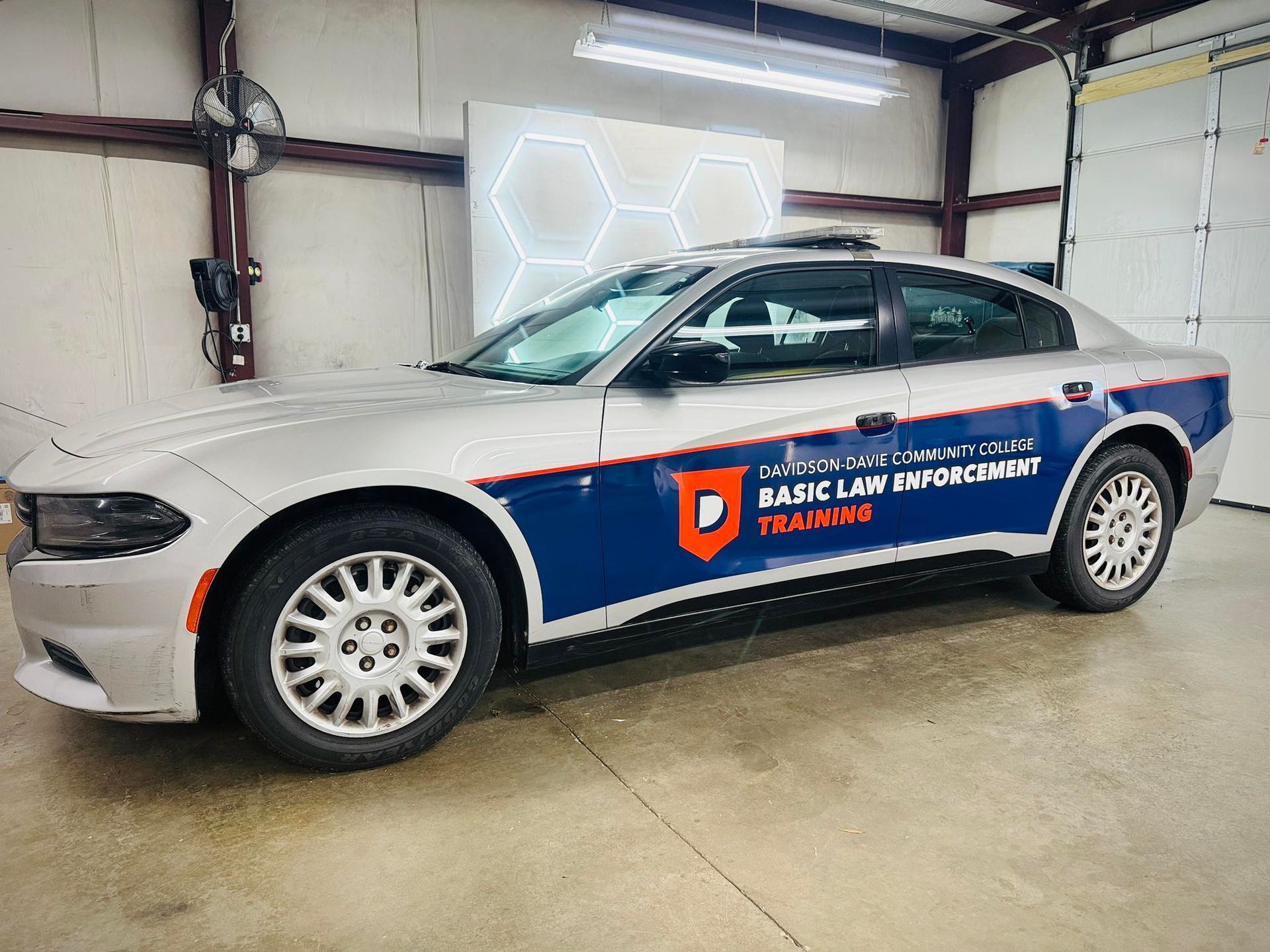 Silver police Dodge Charger with blue side panels, labeled Basic Law Enforcement Training inside a garage.