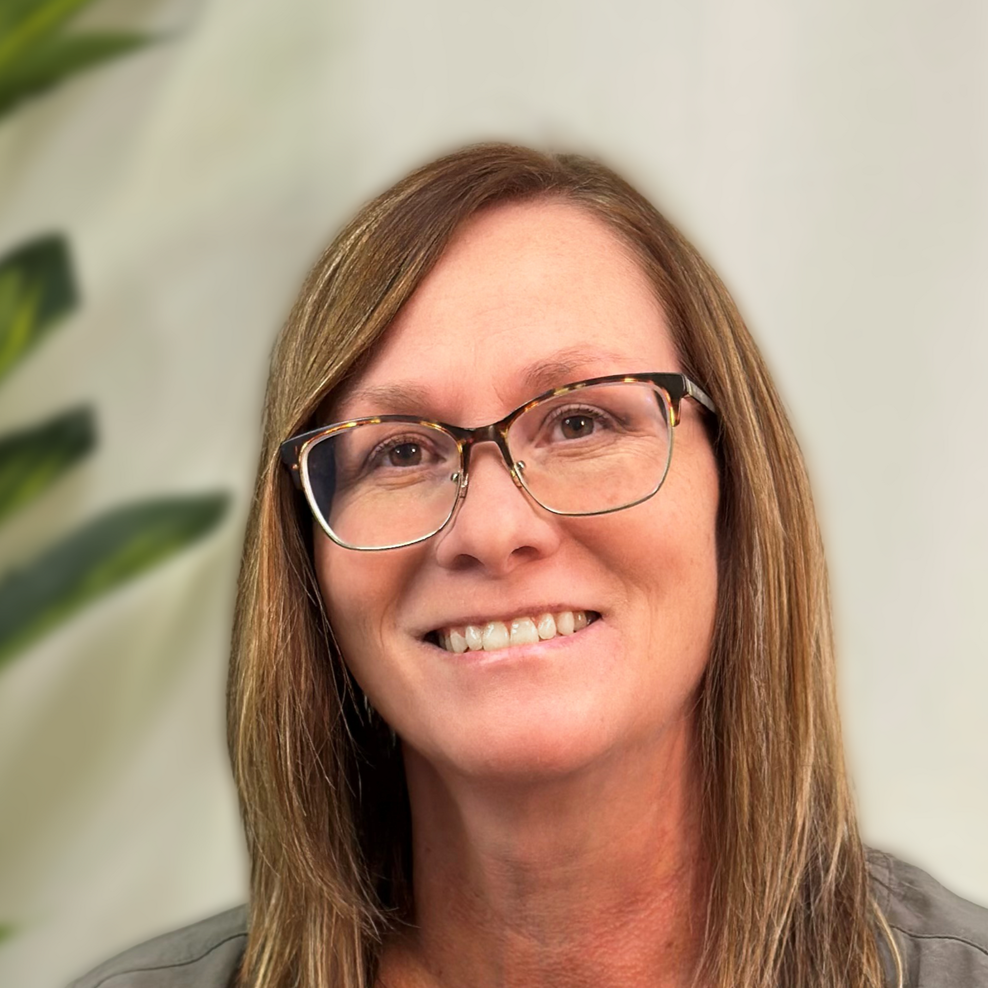 Woman wearing glasses smiles at the camera, wearing a black top against a blurred blue background.