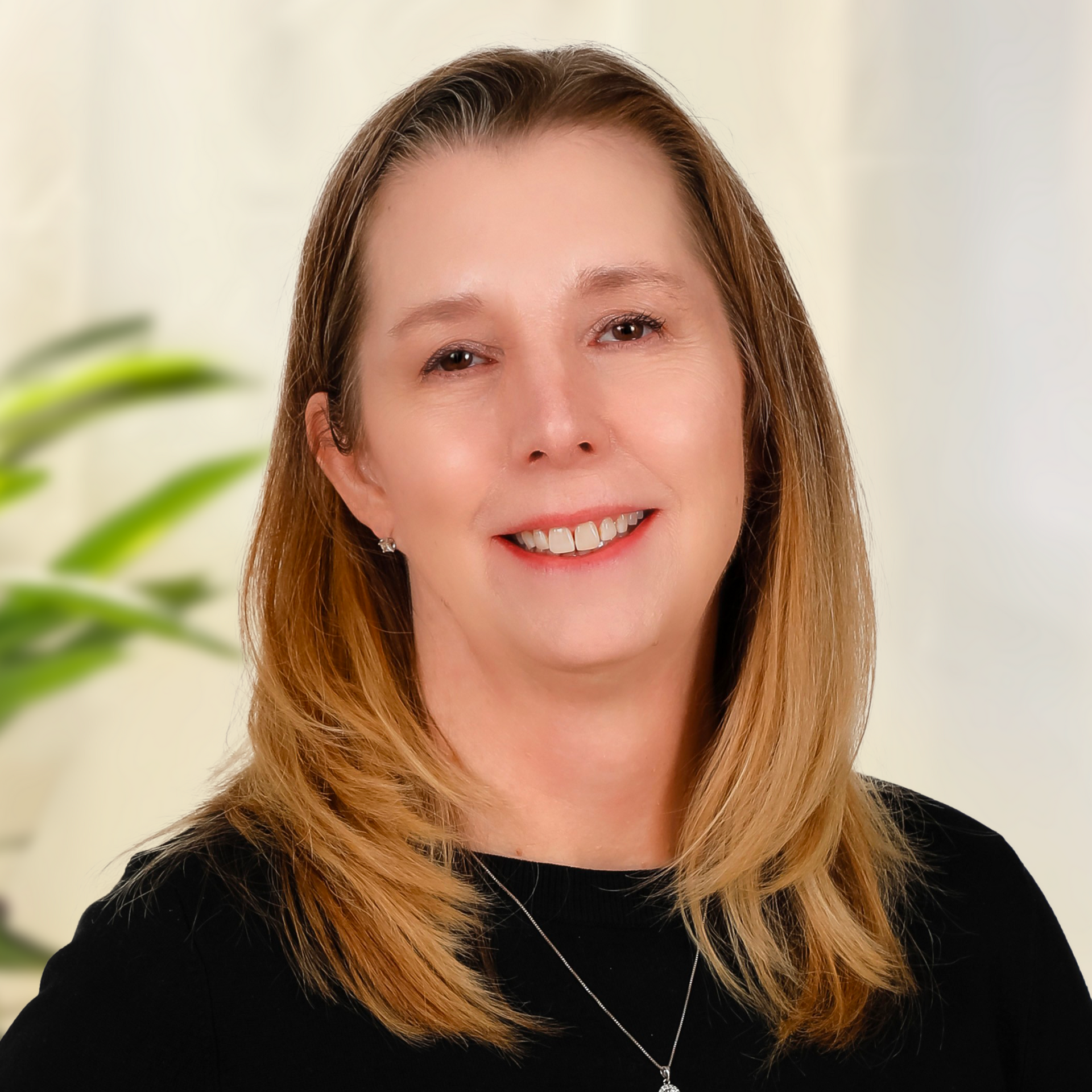Blond woman smiles, wearing a black and white striped top, in front of a dark gray background.