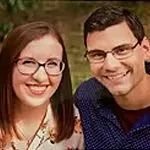 Woman and man smiling, both wearing glasses, outdoors.