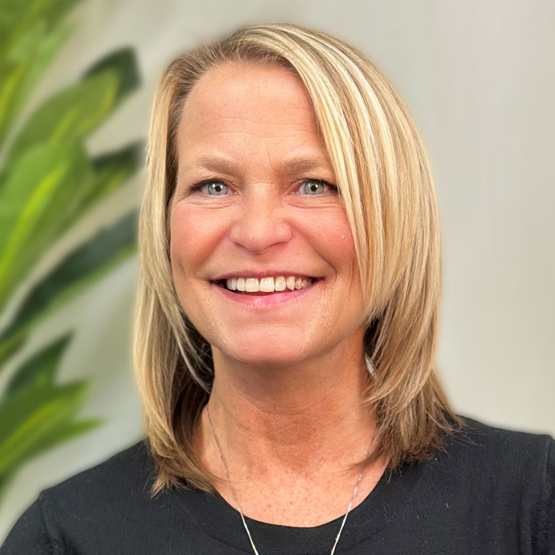 Woman with blonde hair wearing a black turtleneck smiles in front of a gray background.