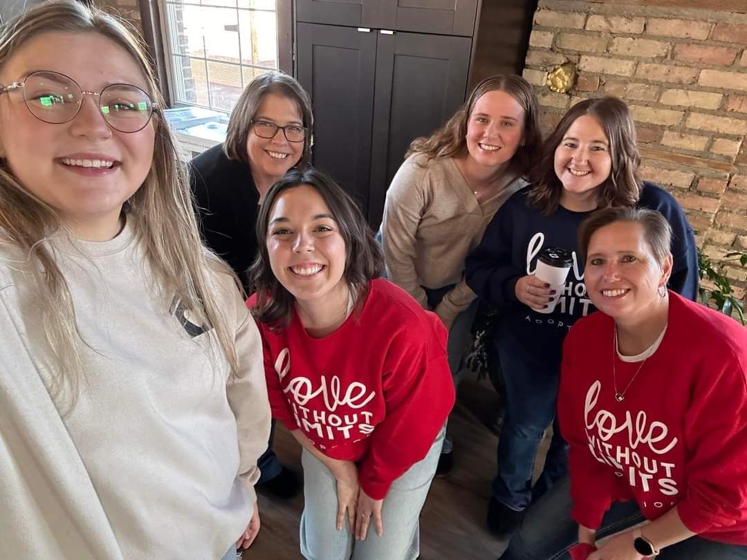 Group of women smiling, posing for a photo. Some wear red 